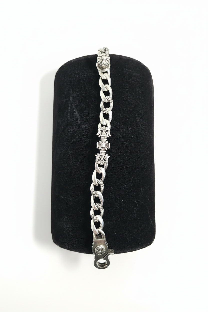 A silver-toned chain bracelet with decorative star and cross motifs, displayed on a black cylindrical velvet jewelry stand over a white faux fur background.